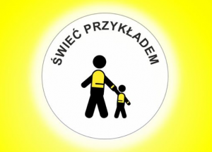 Białe koło na żółtym tle. W górnej części koła napis: ŚWIEĆ PRZYKŁADEM, pod nim dwie postacie ubrane w odblaski i trzymające się za rękę, dorosły i dziecko.