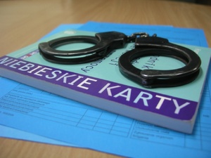 Formularz "Niebieskiej Karty", na którym leży książka z napisem"Niebieskie Karty", na niej leżą kajdanki.