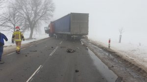 Pora dzienna, silne zamglenie. Po lewej stronie strażak idący w stronę ciężarówki stojącej na całej szerokości jezdni.