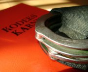 Na pierwszym planie kajdanki, pod nimi kodeks karny z czerwoną okładką.