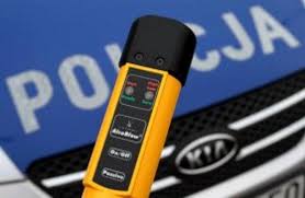 Żółty tester do badania stanu trzeźwości na tle niebieskiej pokrywy silnika radiowozu oznakowanego z napisem POLICJA.