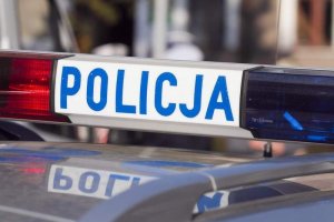 Belka z napisem policja na policyjnym radiowozie. Z lewej strony jest czerwona, z prawej niebieska. Pora dzienna.