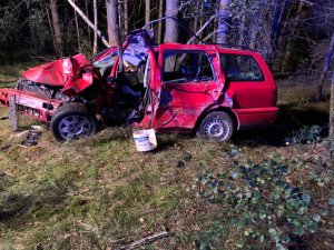Rozbite auto typu kombi koloru czerwonego. W tle las. Pora nocna.