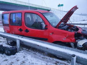 Pora dzienna. Pojazd marki Fiat uczestniczżcy w zdarzeniu drogowym. Pojazd koloru czerwonego. z otwarta pokrywą silnika. W tle jezdnia.