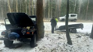 Pora dzienna. Las przy jezdni.  samochód osobowy marki Jeep z uniesioną pokrywą silnika w tle 2 mężczyzn i przyczepka samochodowa.