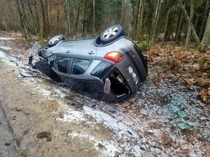 Pora dzienna. droga przez las. W rowie auto osobowe typu suv leżący na dachu. Auto z widocznymi uszkodzeniami pokolizyjnymi.