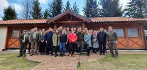 Pora dzienna. Zdjęcie grupowe kilkudziesięciu osób, które uczestniczyły w sadzeniu drzew. W tle drewniany budynek leśniczówki.