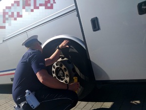 Policjant w trakcie sprawdzania stanu ogumienia autobusu.