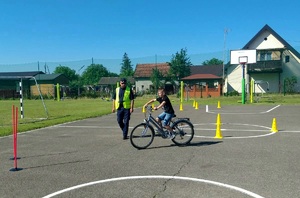 Plac przed szkołą.Chłopiec na rowerze i przeprowadzający egzamin policjant.