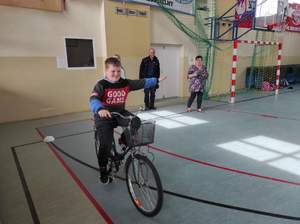 Sala sportowa. W tle policjant, na pierwszym planie chłopiec na rowerze.