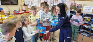Policjantka rozdaje dzieciom książeczki na ratunek Poli w sali lekcyjnej.