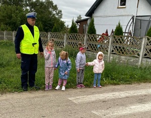 Policjant i czworo dzieci stojących przed przejściem dla pieszych.