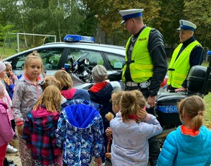Grupa dzieci przedszkolaków, w tle 2 policjantów ruchu drogowego, radiowóz i motocykl.
