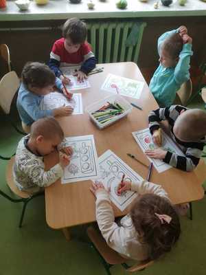 Przedszkolaki w trakcie kolorowania siedzą przy stoliku.