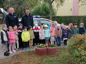 Zdjęcie grupowe przedszkolaków z policjantami, za nimi stoi radiowóz.