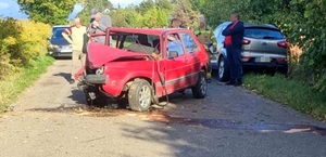 Pora dzienna. na środku jezdni stoi rozbity czerwony samochód osobowy marki VW. W tle 2 inne pojazdy osobowe i kilkoro ludzi, wśród nich strażak.