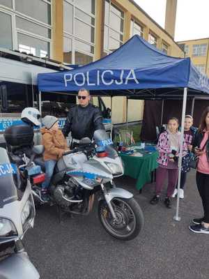 namiot profilaktyczny a przed nim policjant ruchu drogowego wraz z motocyklem i siedzącym na nim dziecku