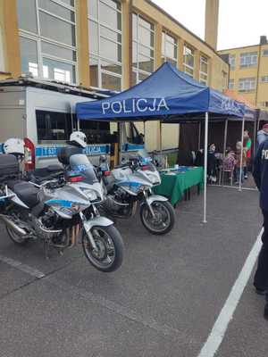 stoisko profilaktyczne, dwa motocykle policyjne za nimi namiot profilaktyczny policji w tle inne namioty