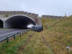 ujęcie z oddali widoczne są ślady pojazdu zostawione na trawie, wiadukt i leżący przed nim bus