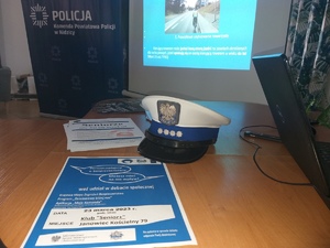 Na pierwszym planie czapka policjanta ruchu drogowego, plakat informujący o debacie, ulotki. W tle ekran z wyświetlonym slajdem.