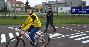 Miasteczko rowerowe. Na pierwszym planie zawodnik na rowerze. W tle policjant.
