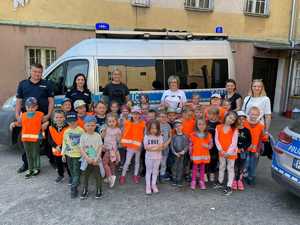 Zdjęcie grupowe. Policjantka i policjant z grupą dzieci. Za nimi bus policyjny.