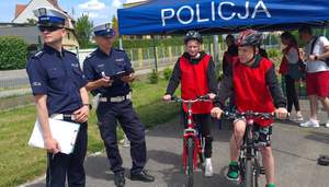 Niebieski namiot z napisem policja. Przed nim stoi 2 policjantów i dzieci na rowerach.