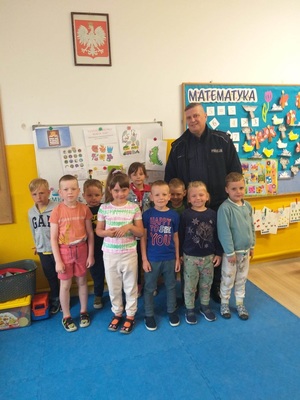 Policjant z grupą dzieci w wieku przedszkolnym stoją w sali.