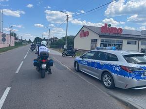 Pora dzienna. Droga A na niej policjant na motocyklu i radiowóz. W tle motocykliści.
