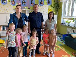 Sala szkolna. Policjant i stojące obok niego 2 nauczycielki i kilkoro dzieci.