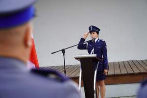 Policjantka prowadząca uroczystość, stojąca za mównicą i oddająca honor.