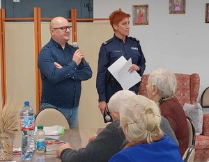 Spotkanie w ŚDS w Janowcu Kościelnym. Policjantka i mężczyzna stoją a przed nim siedzą seniorzy.