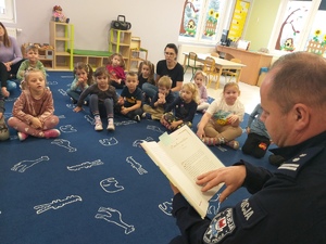 Policjant czyta bajki przedszkolakom siedzącym na dywanie.