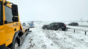 Miejsce kolizji na drodze ekspresowej S7. zaśnieżona droga. Na pierwszym planie żółty pojazd pomocy drogowej. W tle rozbite auto osobowe i radiowóz policyjny,