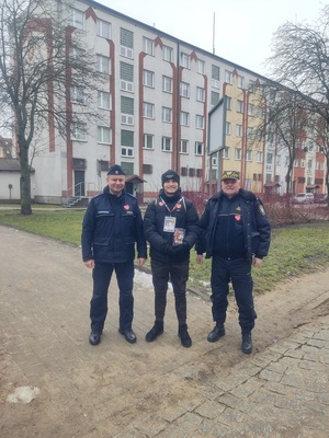 Funkcjonariusz Policji i Straży Miejskiej z wolontariuszem WOŚP, W tle blok.