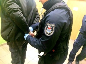 Policjant zakłada kajdanki zatrzymanemu mężczyźnie.