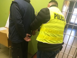 Policjant zakłada kajdanki zatrzymanemu mężczyźnie.