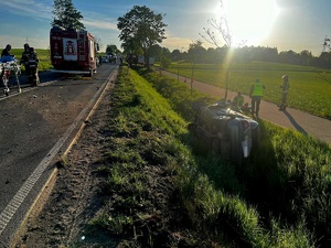 Rozbite auto w rowie. Obok niego stoją służby ratunkowe. W tle na drodze stoi wóz strażacki.