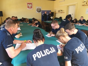 Policjanci siedzący przy stołach podczas odprawy do służby.