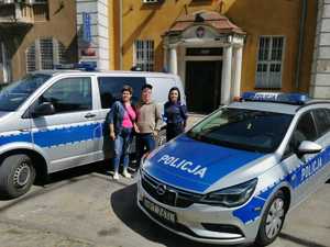 Policjantka, młody mężczyzna i jego mama stojący między radiowozami. W tle budynek Komendy.