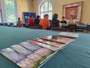 Świetlica KPP w Nidzicy. Uczniowie siedzący przy stole przykrytym zielonym obrusem. Na stole leżą gazetki, ulotki.