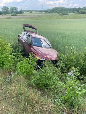 Miejsce wypadku drogowego ze skutkiem śmiertelnym. Auto koloru bordowego rozbite na skutek zderzenia znajdujące się na trawie poza droga.