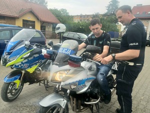 Młody mężczyzna siedzący na motocyklu . obok stoi policjant i drugi motocykl.