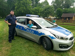 Policjant stojący przy radiowozie, a z pojazdu wygląda dziecko.