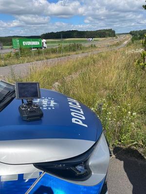 Dron unoszący się w powietrzu. Na pierwszym planie radiowóz policyjny.