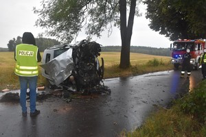 Miejsce wypadku drogowego. Policjant stojący przy pojeździe leżącym na boku.