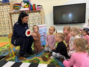 Policjantka i grupa przedszkolaków podczas spotkania na temat bezpieczeństwa w ruchu drogowym.