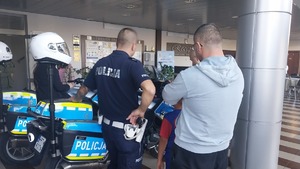 Policjanci promujący zawód policjanta i bezpieczeństwo w ruchu drogowym na stoisku profilaktycznym.