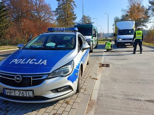 Policjant i ITD podczas kontroli drogowej. Na pierwszym planie radiowóz w tel pojazd osobowy.