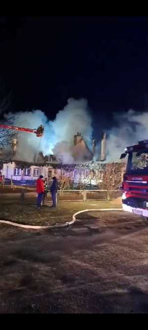 Pożar Szkoły Podstawowej w Szkotowie. Palący się budynek i służby ratunkowe - pojazdy i osoby.